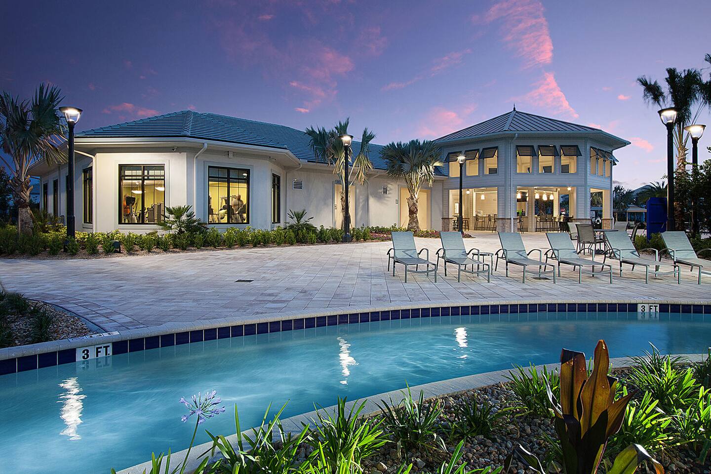 Resort clubhouse pool at dusk with loungers and lit fitness center